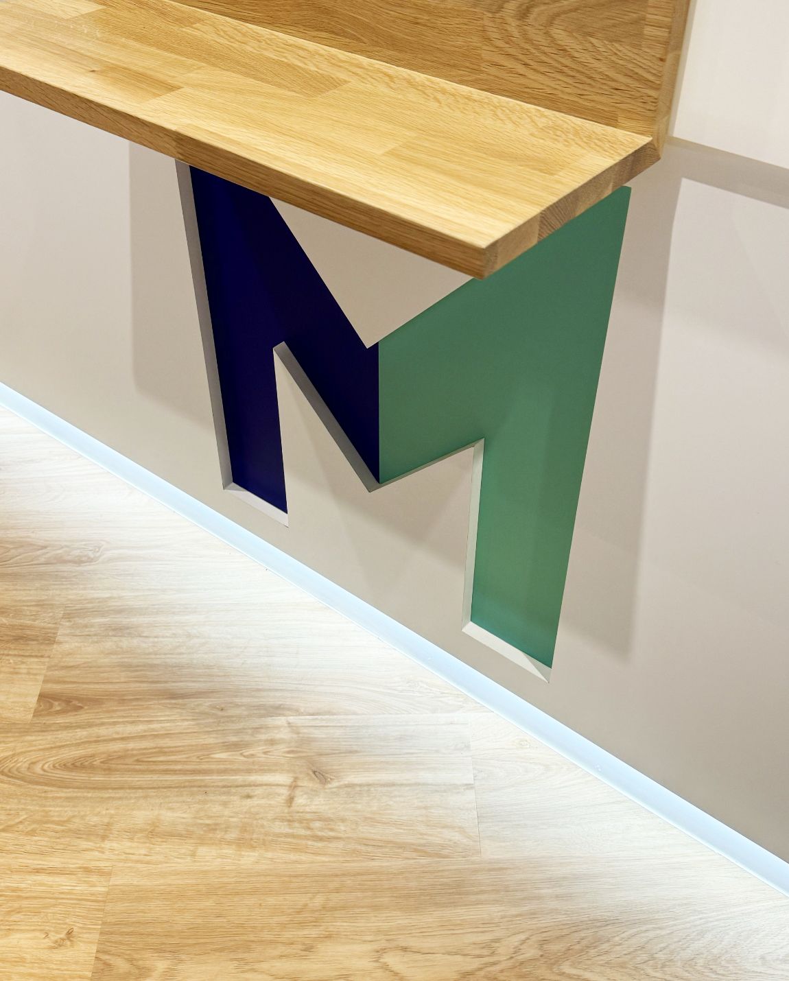 Comptoir en bois sur un mur blanc avec une découpe en « M » bleue et verte.