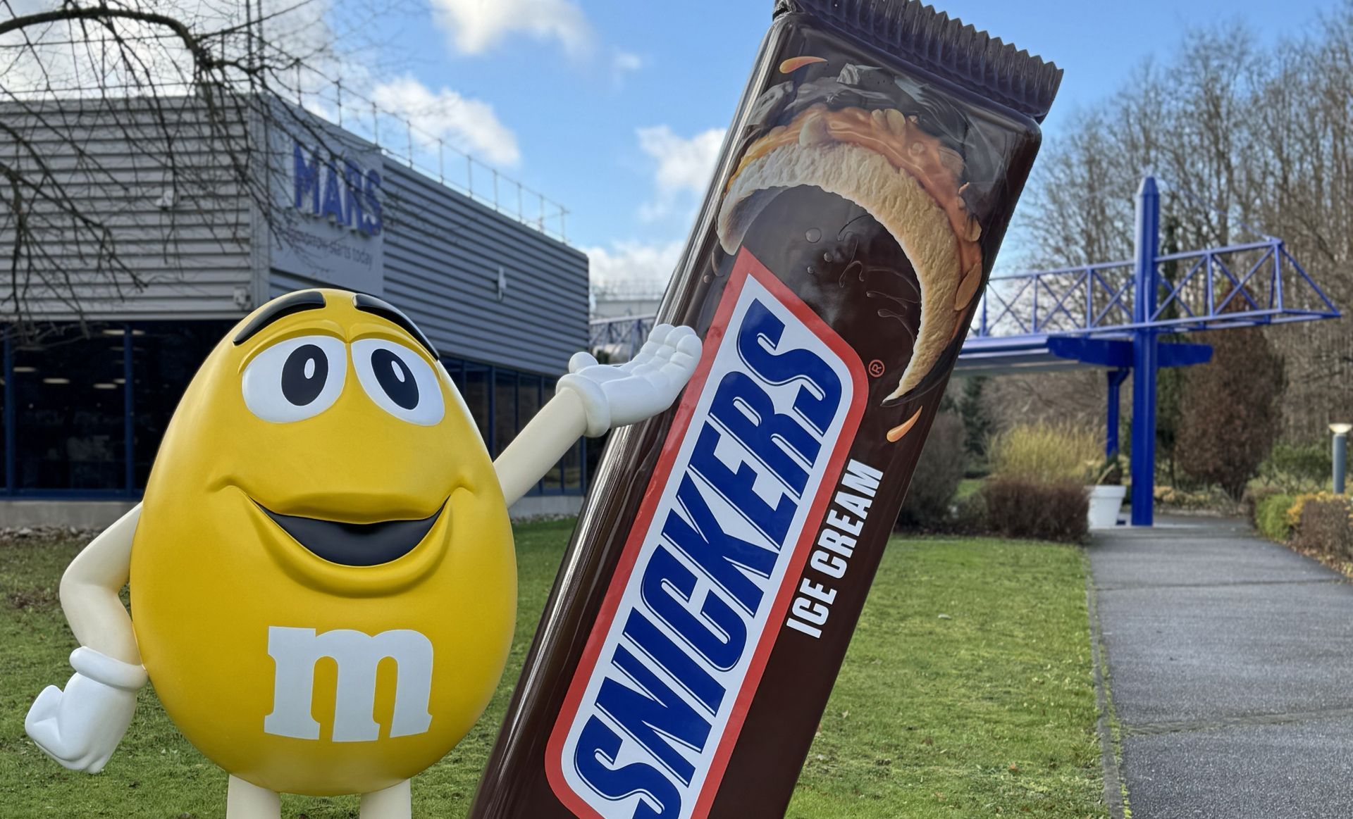 Personnage M&M jaune avec une barre de crème glacée Snickers à l'extérieur du bâtiment Mars.