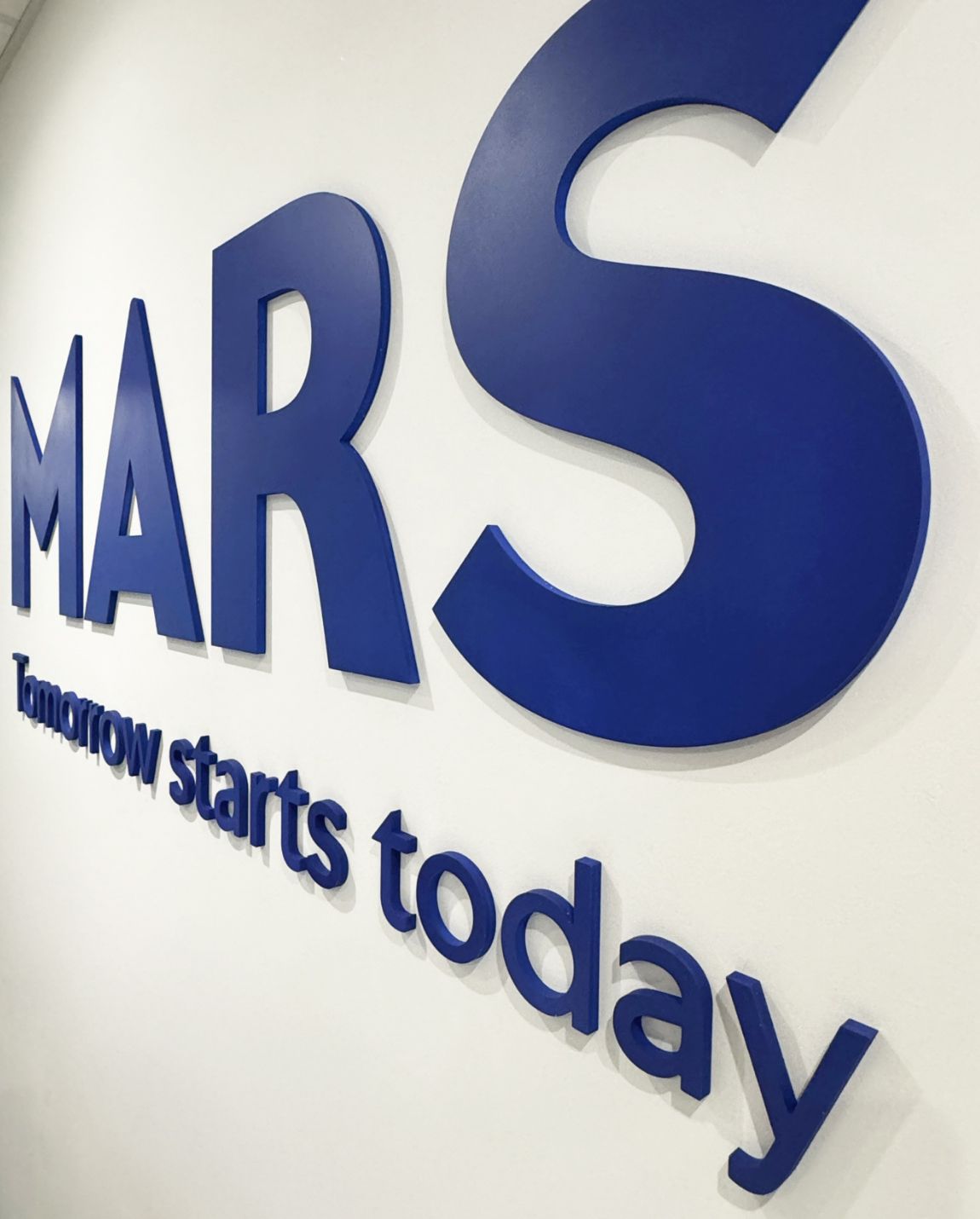 Logo bleu « MARS » avec « Demain commence aujourd'hui » sur un mur blanc.