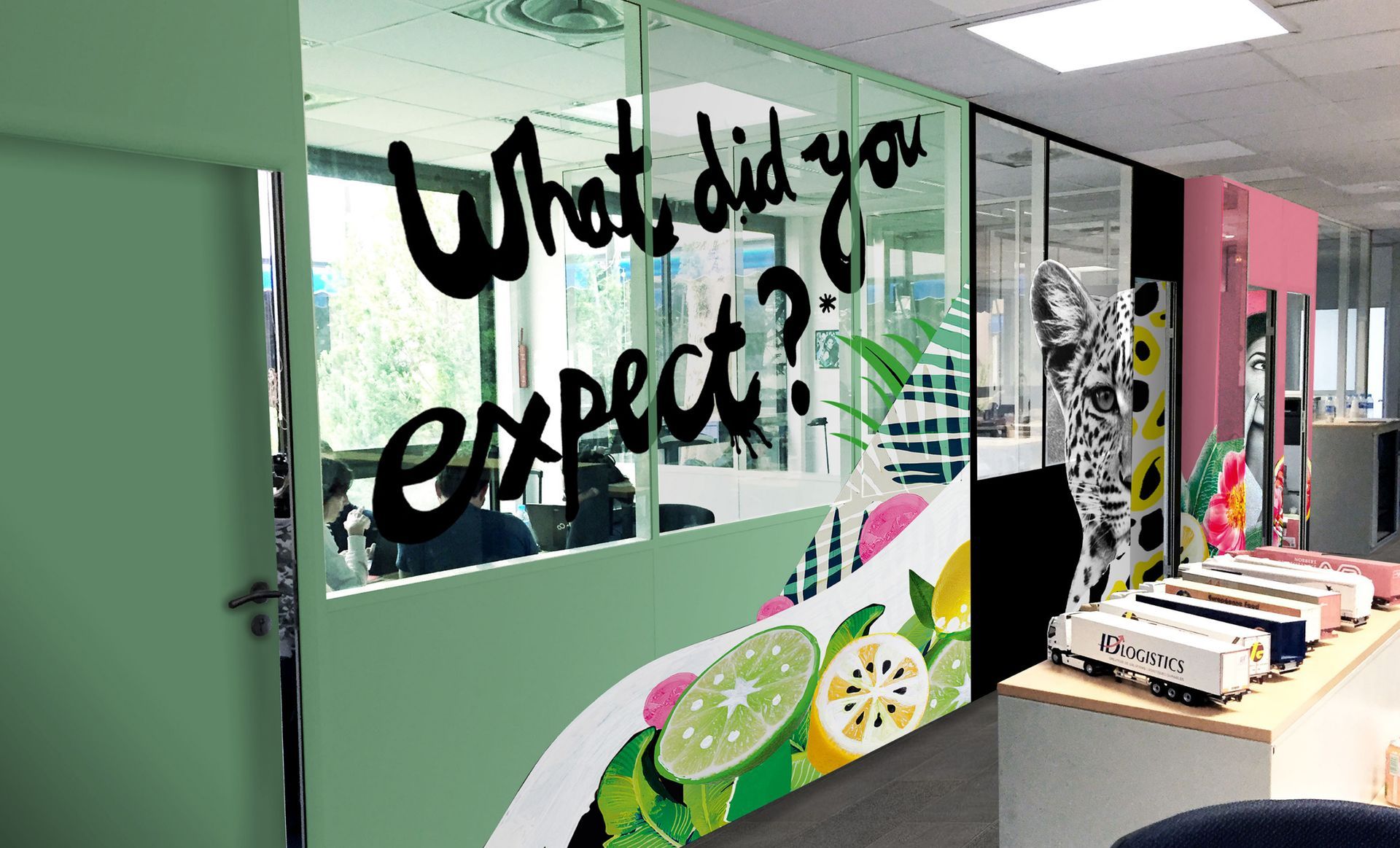 Espace de bureau avec des murs en verre, avec des graffitis « Qu'attendiez-vous ? » et des motifs de fruits colorés.