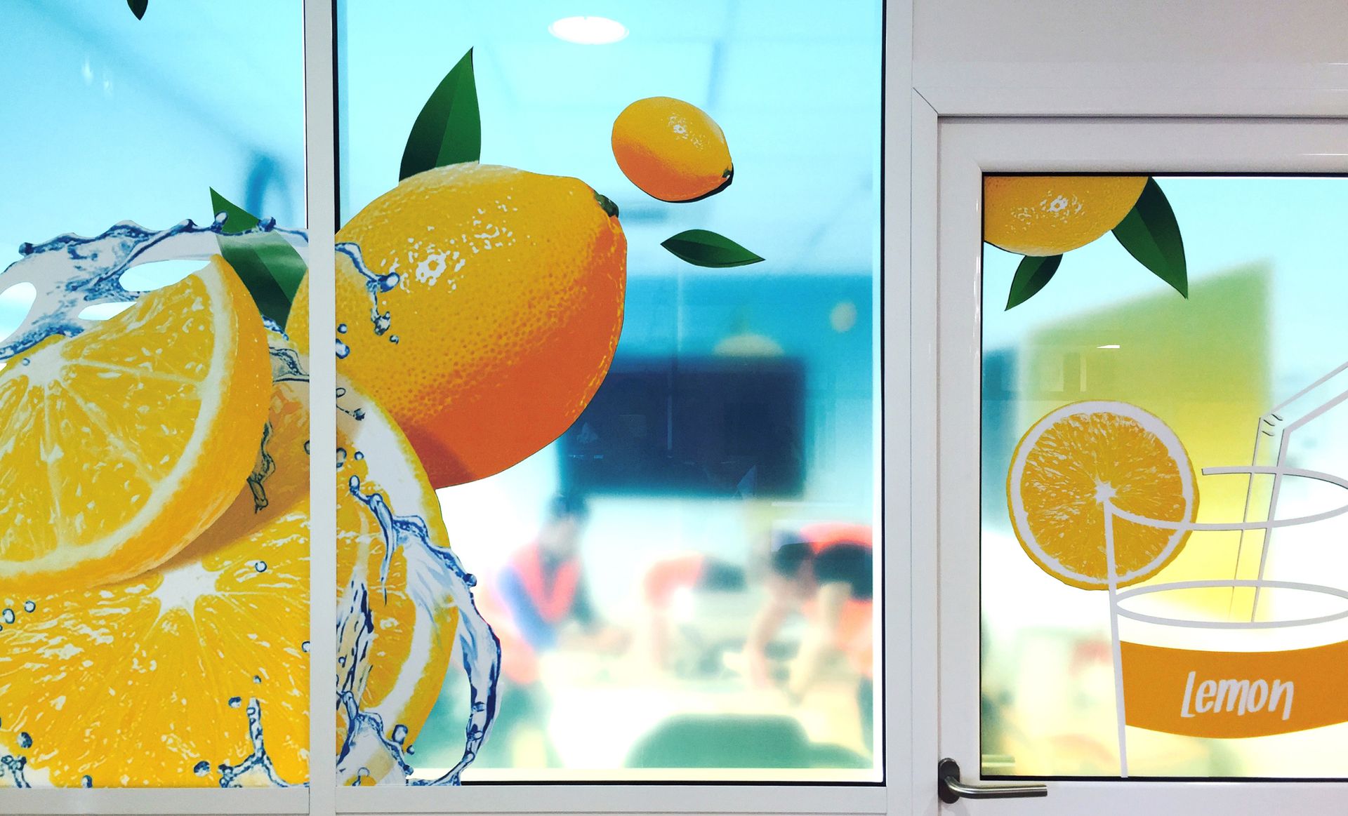Fenêtre décorée de citrons et d'éclaboussures d'eau, intérieur de café visible, teinte bleue.