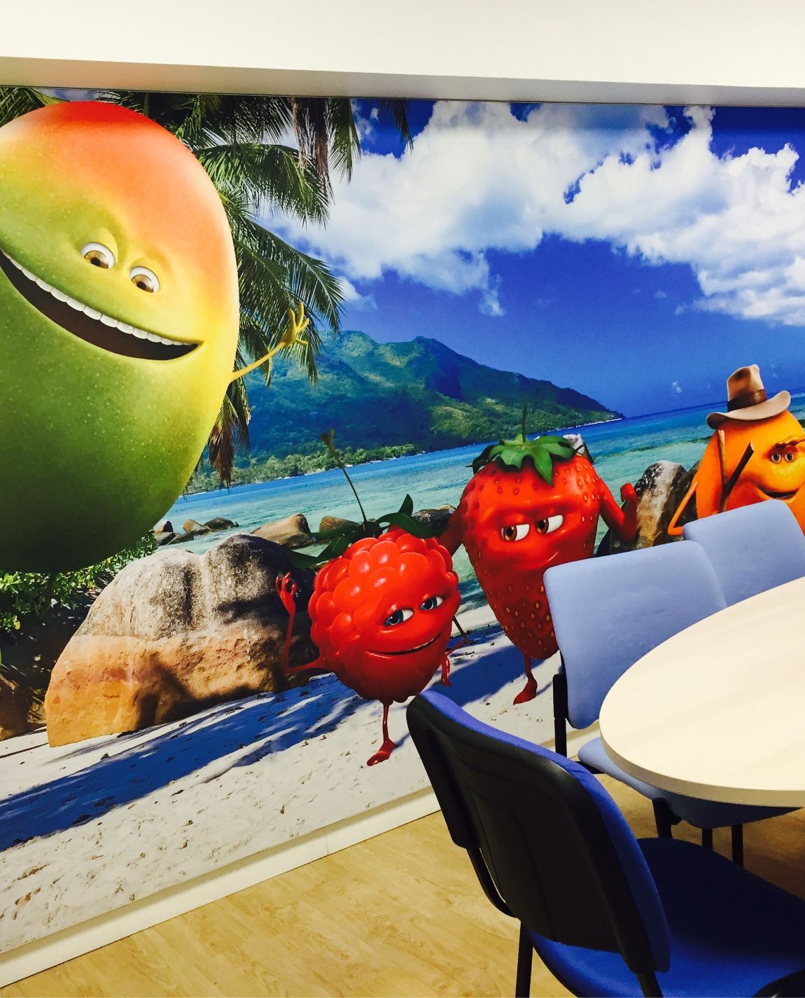 Peinture murale de personnages de fruits souriants sur une plage : mangue, fraises, orange, avec un paysage tropical.
