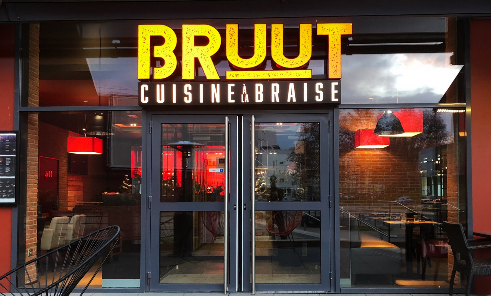 Entrée du restaurant BRUUT Cuisine Braise avec enseigne jaune illuminée, portes vitrées et accents rouges.