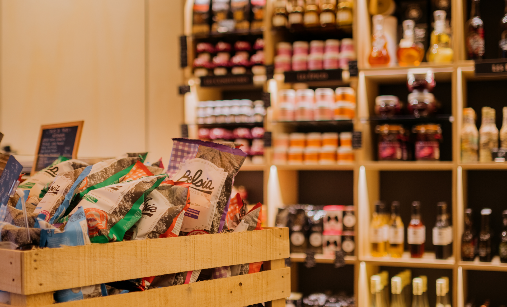 Caisse en bois remplie de sacs de collations dans un magasin ; étagères de pots et de bouteilles en arrière-plan.