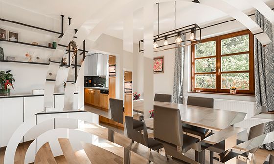 Salle à manger moderne avec table, chaises, fenêtre et cuisine visibles à travers la porte.