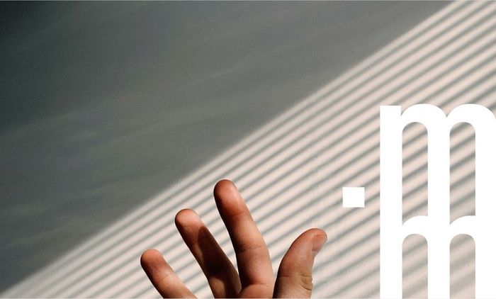 Main tendue vers un logo blanc contre un mur avec des ombres diagonales.
