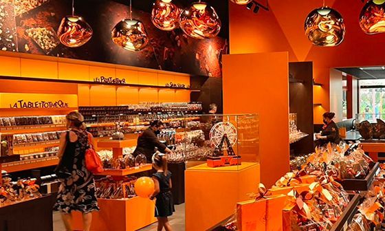 À l'intérieur d'une boutique à thème orange brillamment éclairée, les clients parcourent les présentoirs de chocolat.