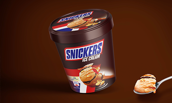 Pot de glace Snickers avec une boule sur une cuillère, fond marron.