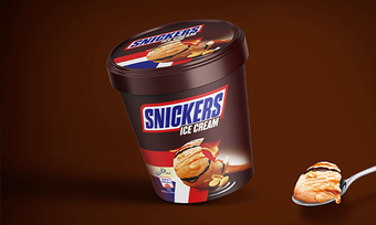 Pot de glace Snickers avec une boule de glace sur une cuillère ; fond marron.