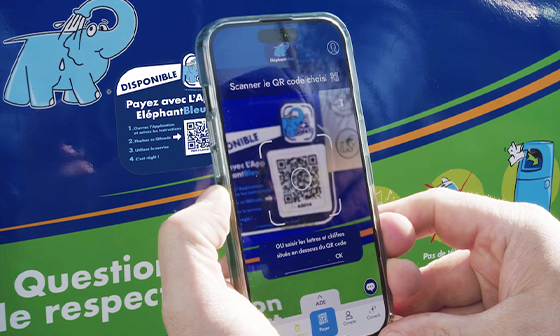 Une personne scanne un code QR avec un téléphone, une poubelle de recyclage bleue avec un logo d'éléphant en arrière-plan.