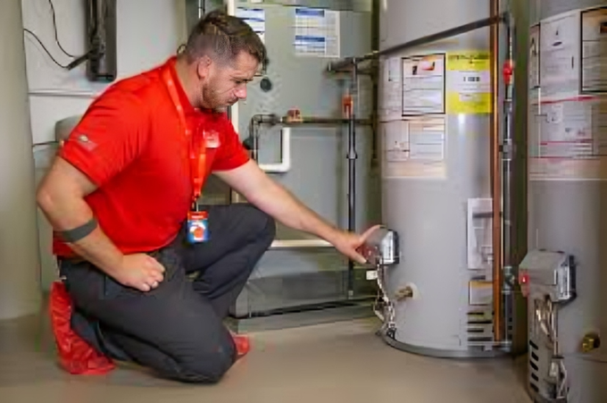 Technician in red uniform inspecting a residential water heater unit.
