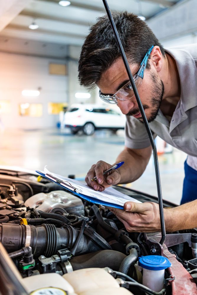 A Man Is Looking Under The Hood Of A Car And Writing On A Clipboard — MB Automotive In Garbutt, QLD