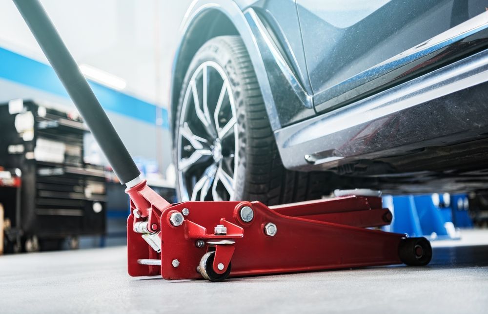 A Red Car Jack Is Sitting Under A Car In A Garage — MB Automotive In Garbutt, QLD