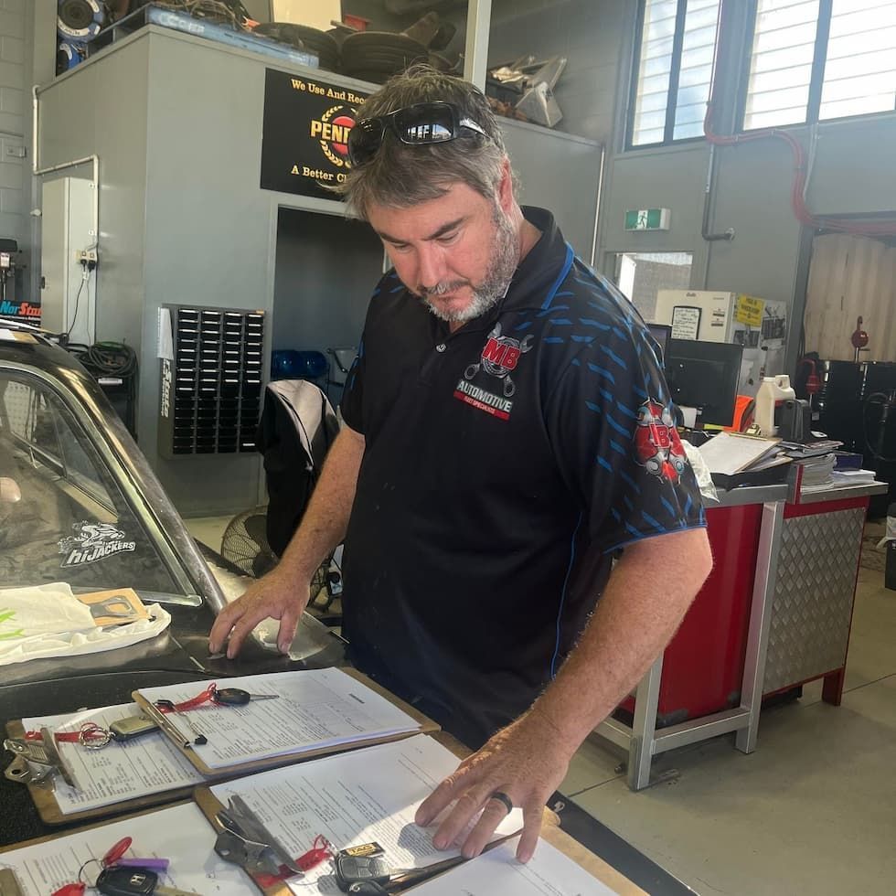 A Man With a Beard and Sunglasses on His Head Reviews Paperwork on Clipboards in an Automotive Works