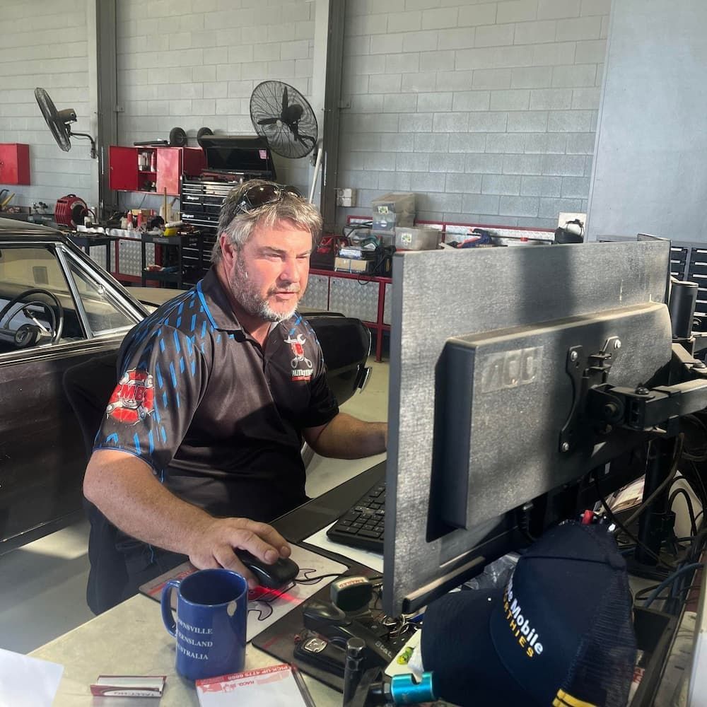 A Man in a Mechanic's Polo Shirt Works at a Computer in a Garage
