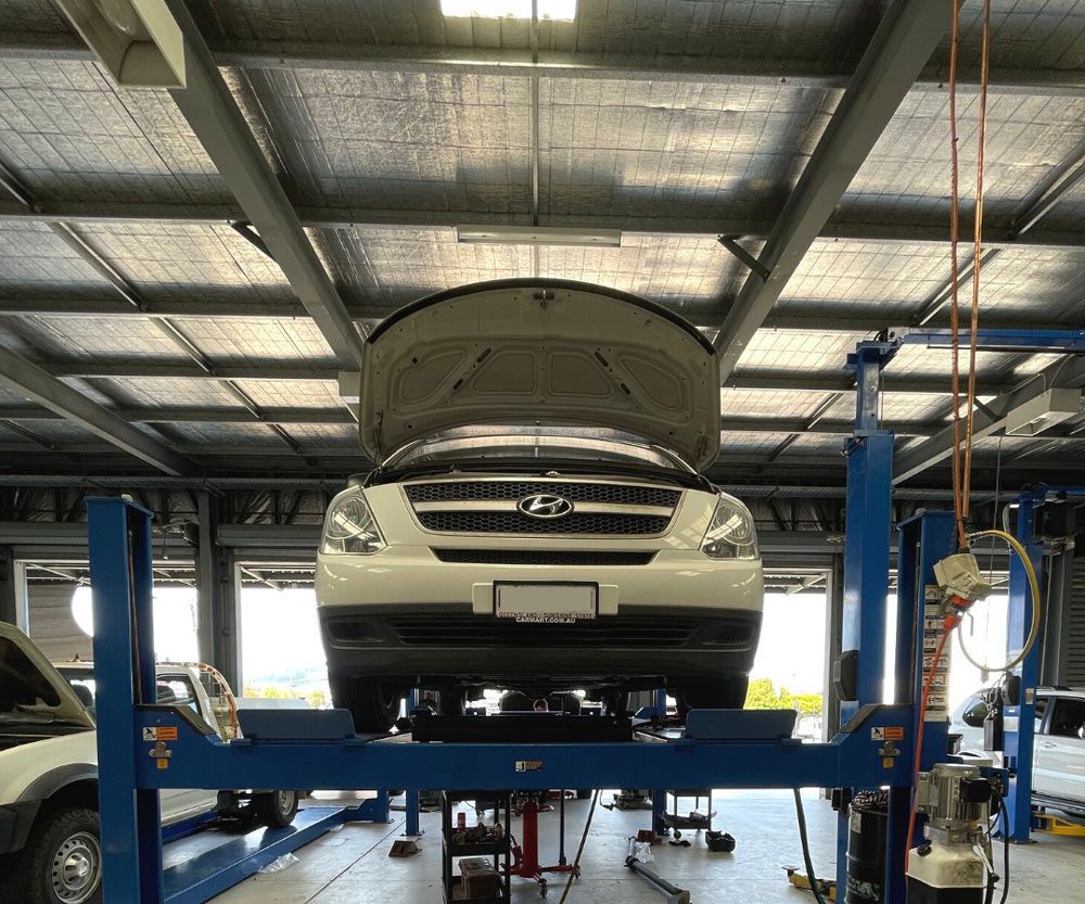 A White Car With The Hood Up Is On A Lift In A Garage — MB Automotive In Garbutt, QLD