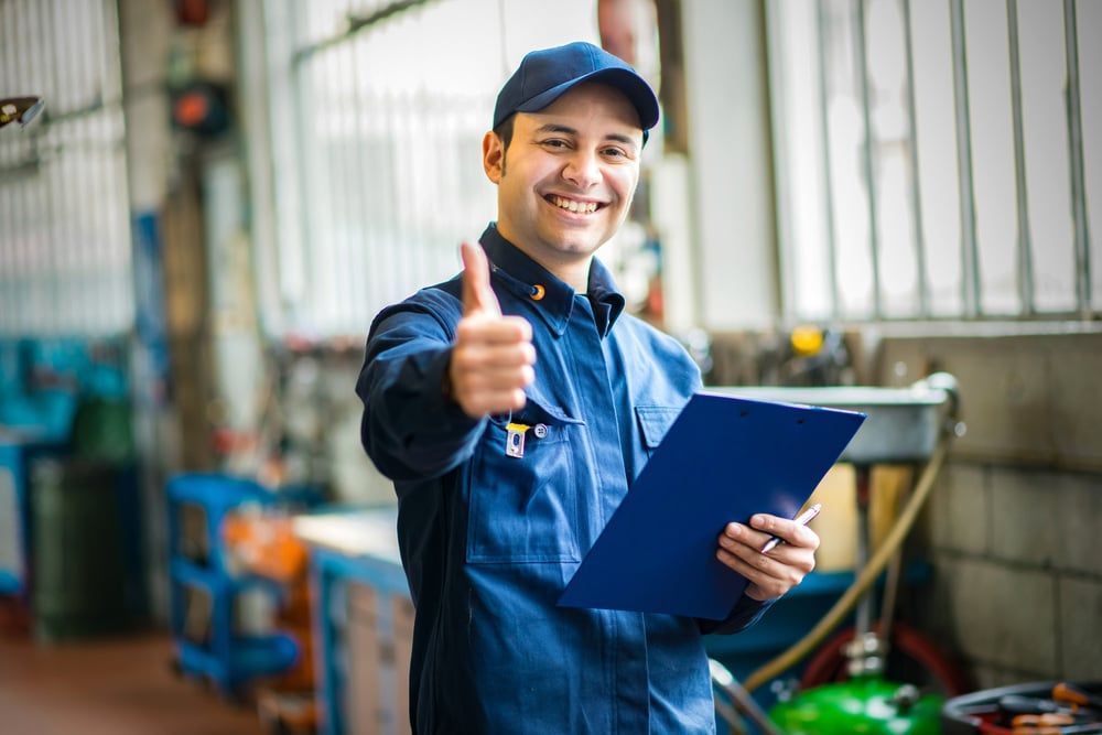 A Mechanic Is Giving A Thumbs Up While Holding A Clipboard In A Garage — MB Automotive In Garbutt, QLD