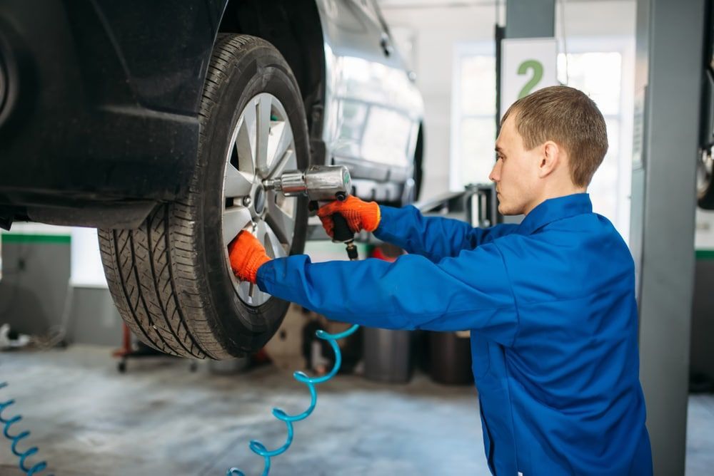 A Man Is Changing A Tyre On A Car In A Garage — MB Automotive In Garbutt, QLD