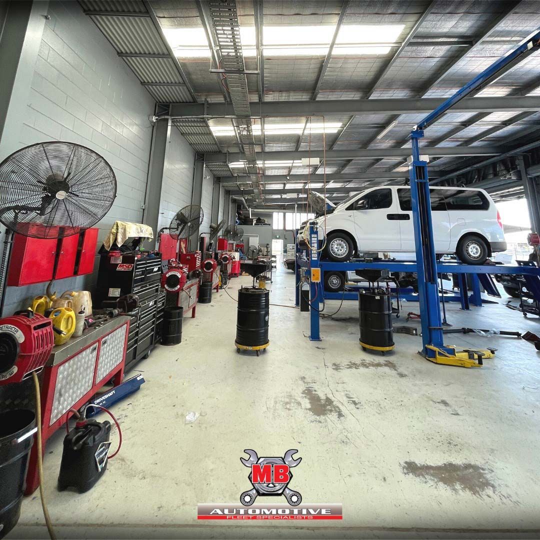 A Man Is Changing A Tyre On A Car In A Garage — MB Automotive In Garbutt, QLD