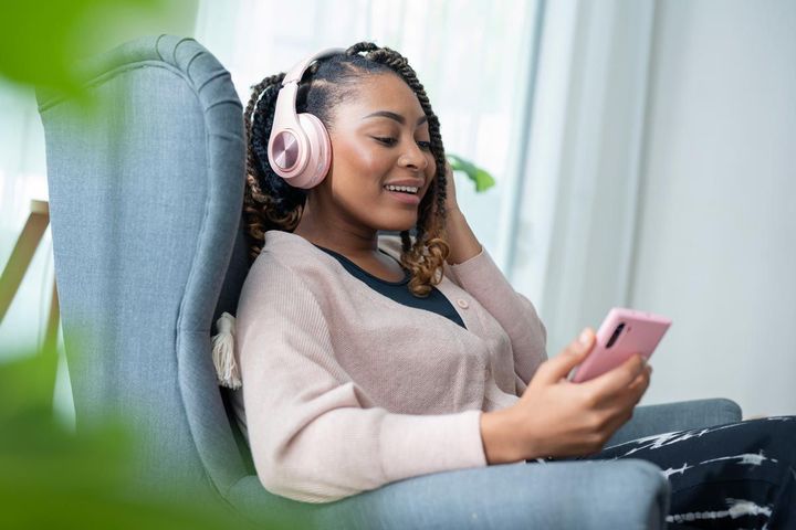 A woman is sitting in a chair wearing headphones and looking at her phone.