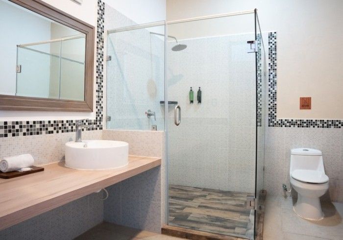 Baño moderno con ducha de cristal, lavabo suspendido e inodoro junto a detalles de azulejos de mosaico.