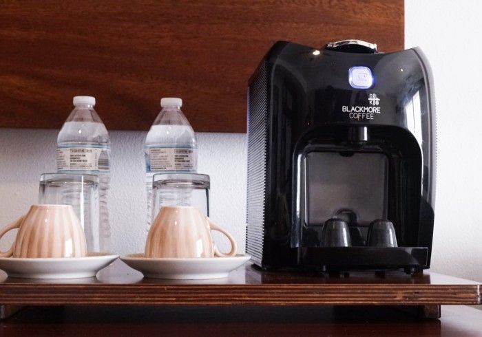 Estación de café con máquina Black & White, tazas, botellas de agua y servilletas sobre un mostrador de madera.