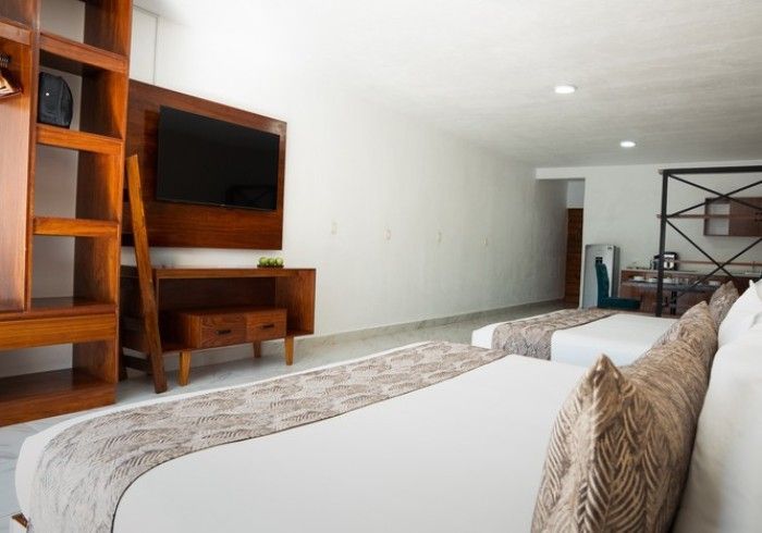 Dormitorio moderno con cama blanca, mueble de TV de madera, estanterías empotradas y alfombra estampada.