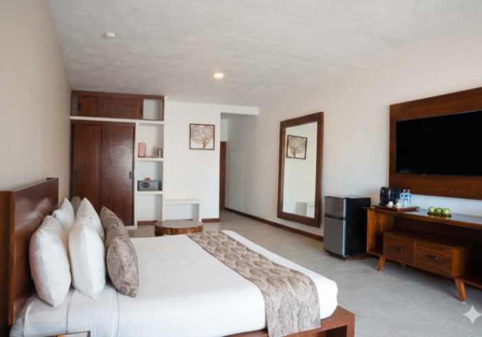 Habitación amplia con cama, televisor, escritorio, espejo grande y decoración en tonos beige.