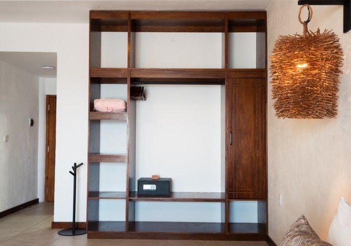 Estanterías y armario empotrados de madera en una habitación minimalista, con una lámpara colgante de mimbre a la derecha.