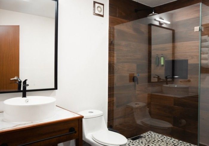 Baño moderno con lavabo con mueble, inodoro y ducha con mampara de cristal, suelo de azulejos con aspecto de madera y guijarros.