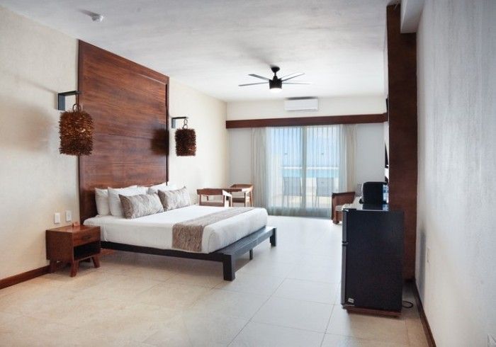 Habitación de hotel moderna con cama king, pared decorativa de madera, ventilador de techo, escritorio y puertas corredizas de vidrio.