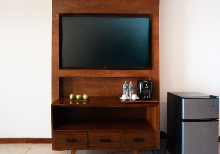 Mueble de televisión de madera con una pantalla en blanco, estantes, cajones y un mini refrigerador al lado en una habitación austera.