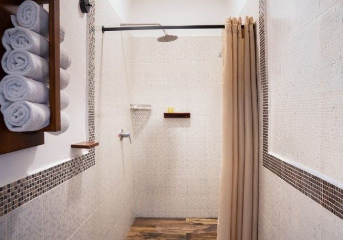 Cabina de ducha estrecha con azulejos, cortina de ducha, estante de pared y toallas dobladas a la izquierda.
