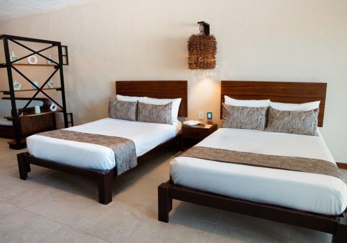 Habitación de hotel con dos camas individuales, sábanas blancas, cabeceros de madera y lámpara de pared de mimbre.