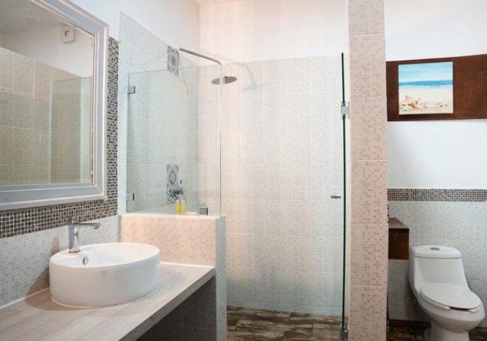 Baño moderno con ducha de cristal, lavabo sobre encimera, espejo e inodoro bajo un cuadro enmarcado en la pared.