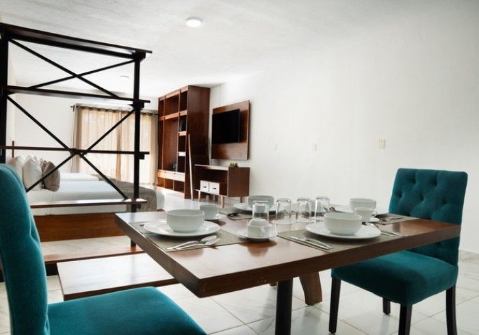 Juego de mesa de comedor con vajilla blanca y sillas color turquesa en una habitación luminosa y moderna.