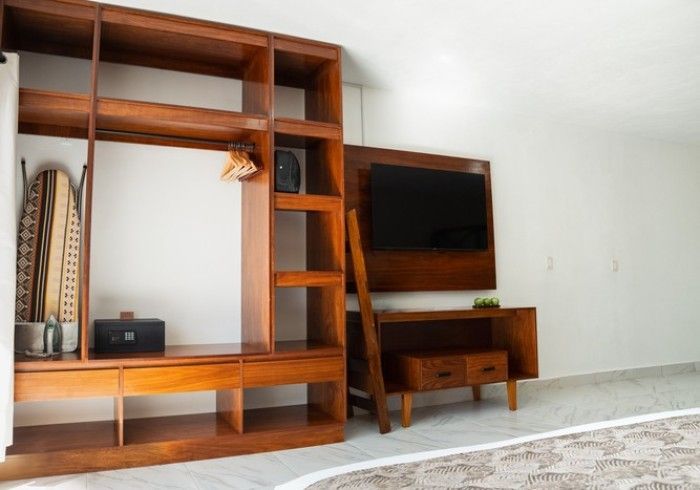 Mueble de pared de madera con televisor, escritorio pequeño y estantes en una habitación escasamente amueblada.
