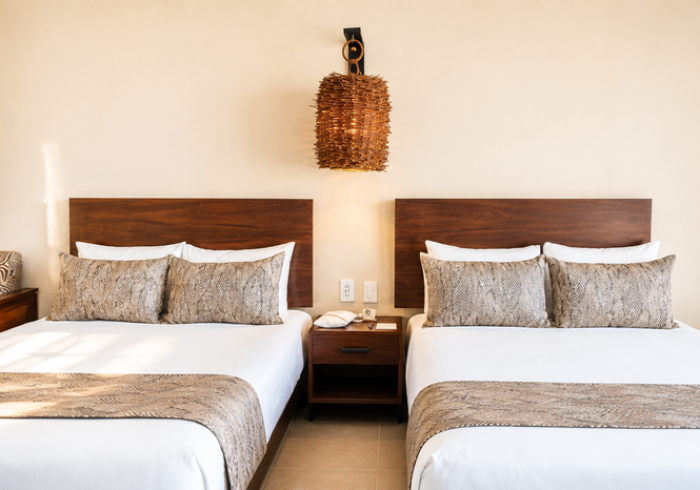Dos camas individuales bien hechas con cabeceros de madera en una sencilla habitación de hotel.