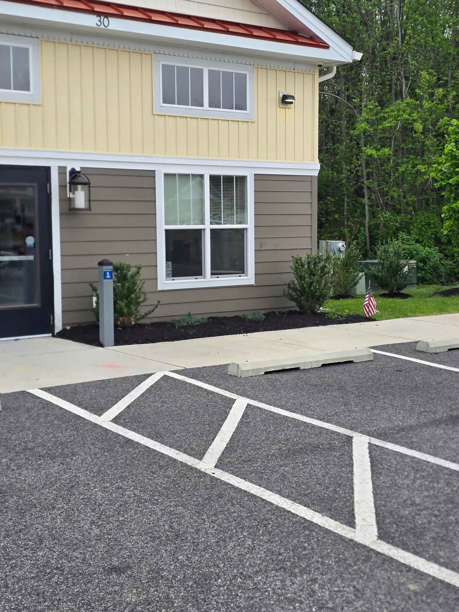 Exterior of a two-story building with yellow and brown siding, a red roof, and a parking lot with marked spaces.