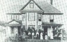 A black and white photo of a family standing in front of a large house.