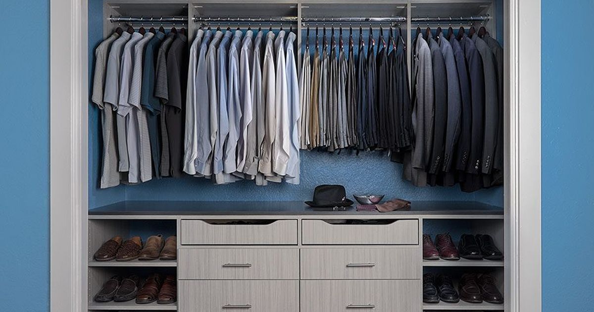 A walk-in closet with hanging clothes, drawers, and shelving for shoes, set against a blue wall.