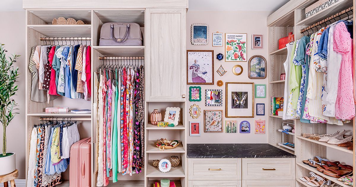 Walk-in closet with neatly organized clothes, decorative wall art, and a pink suitcase; light and bright space.