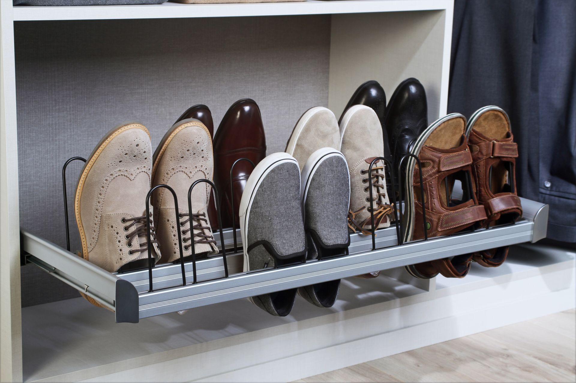 A pull-out metal shoe rack inside a closet, organized with various styles of footwear.