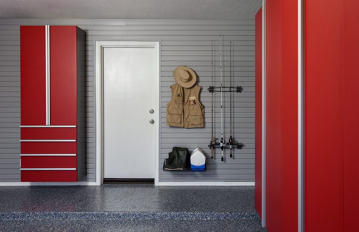 A white door in a garage with grey slat walls, red cabinets, and fishing gear hung on the wall.