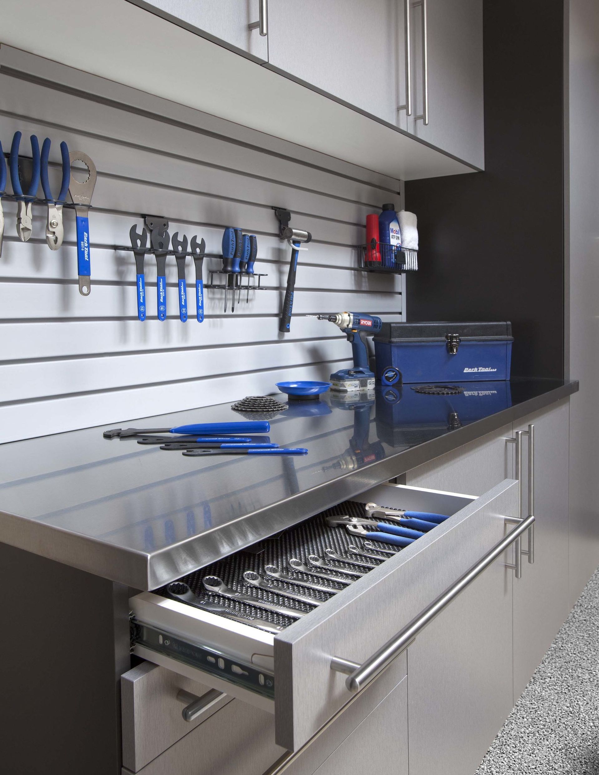 A workspace featuring a stainless steel countertop, a wall-mounted tool storage system, and an open drawer filled with tools.