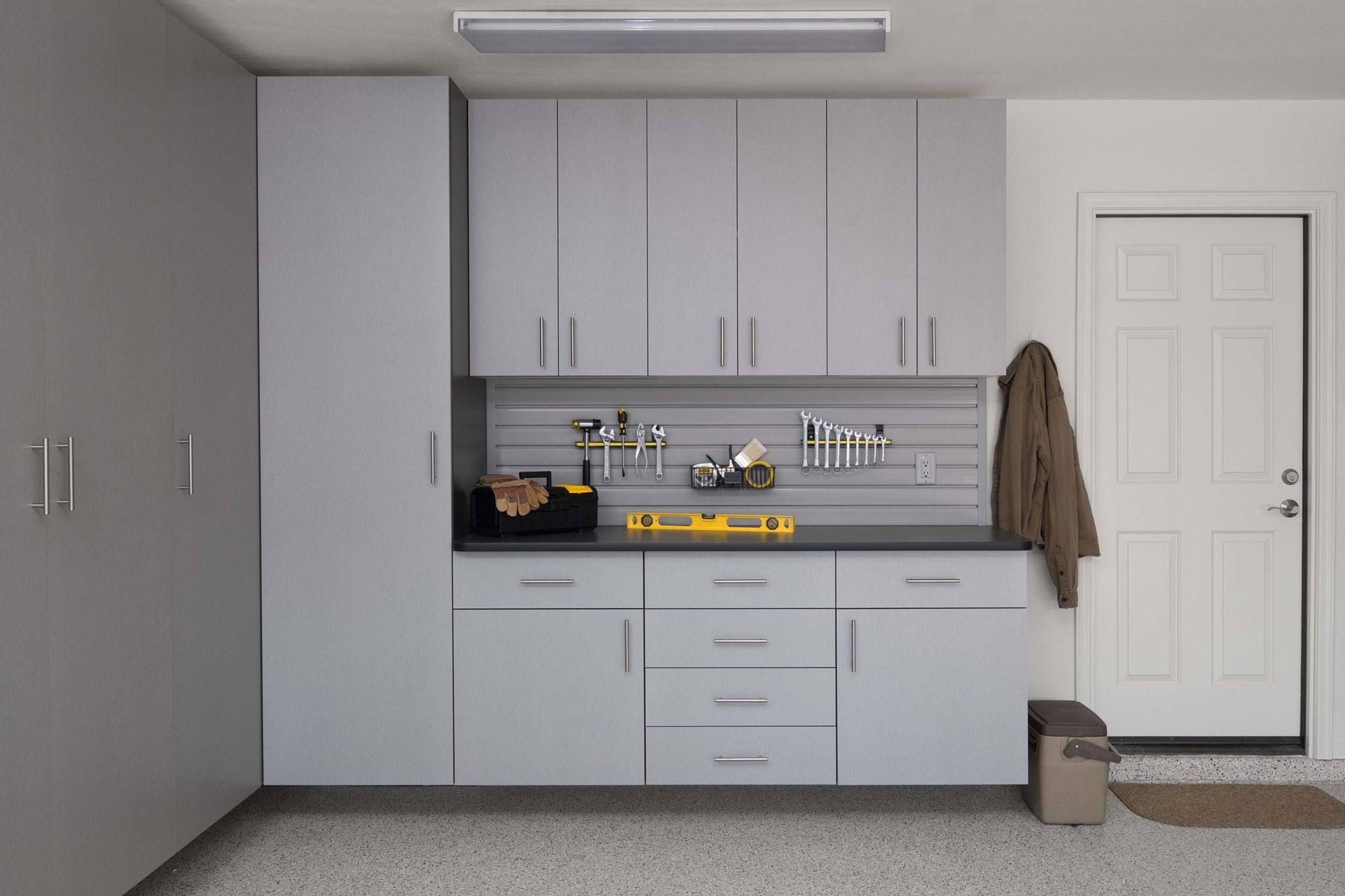Modern light gray storage cabinets and a workbench in a garage with a slat wall organization system for tools.