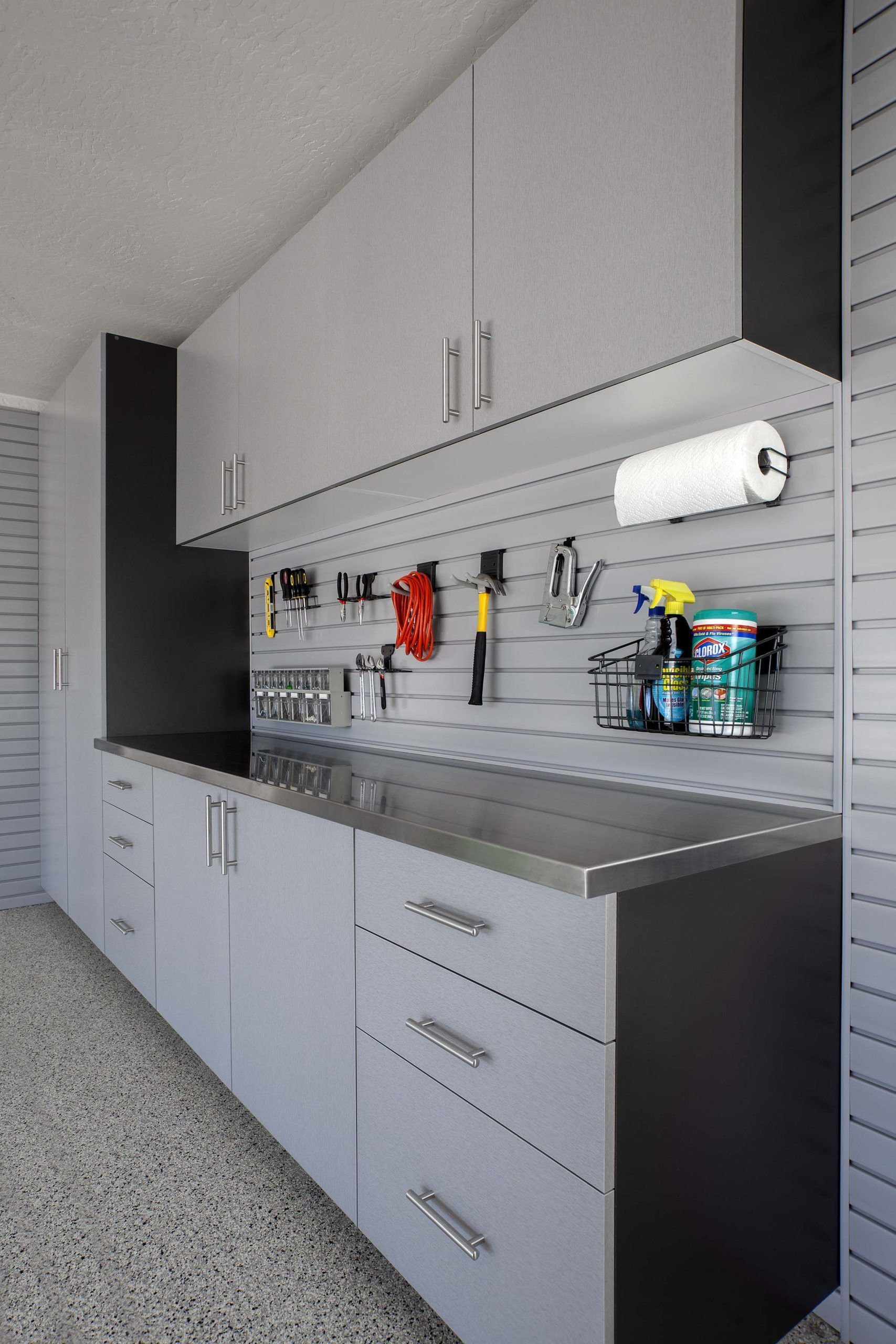 Modern grey garage cabinets and stainless steel counters with a wall-mounted slat wall organizer and storage hooks.