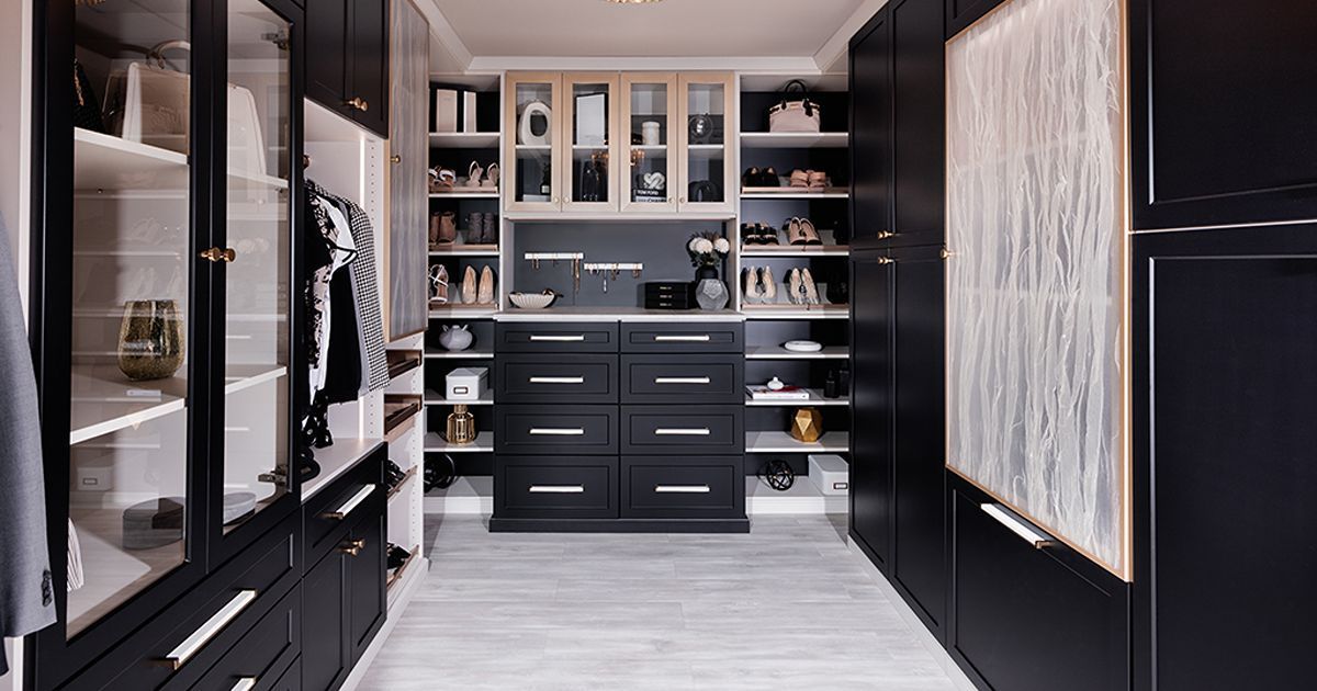 A luxury walk-in closet featuring floor-to-ceiling black cabinetry, open shelving, a central dresser, and light flooring.