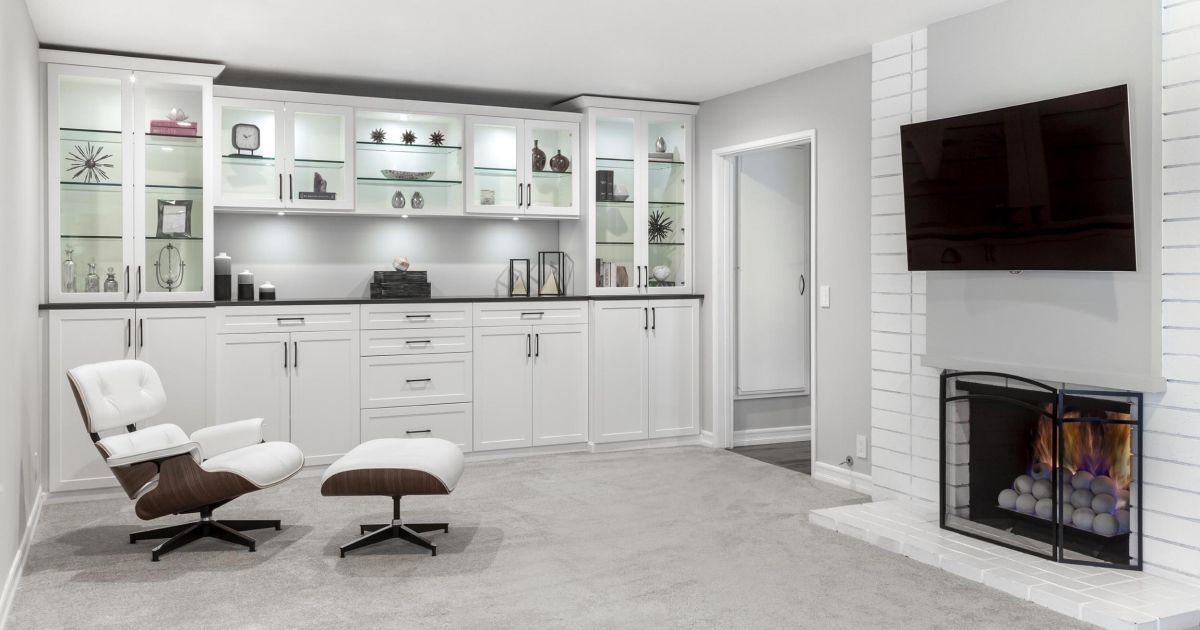 White built-in cabinets and shelves in a living room with a fireplace, a TV, and a lounge chair.