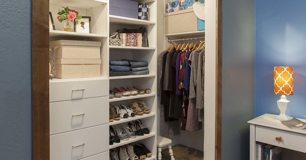 Walk-in closet with clothes, shoes, and boxes organized on shelves. Blue walls and a white nightstand.